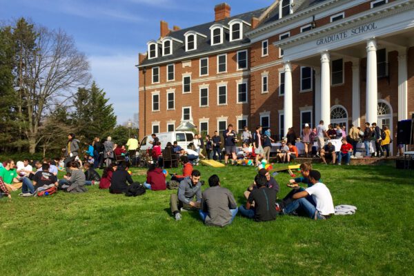 Students sitting outside on the lawn in front of a red-brick campus building.